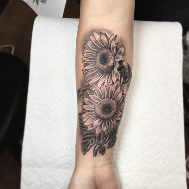 Black and grey forearm tattoo featuring two detailed sunflowers with intricate shading and fine linework for a bold floral design.
