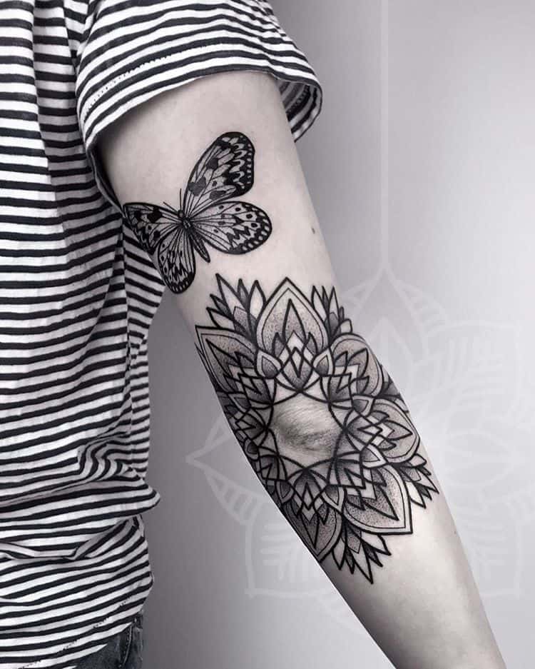 Intricate black and grey butterfly and mandala tattoo on the arm, blending geometric patterns with delicate nature-inspired details.