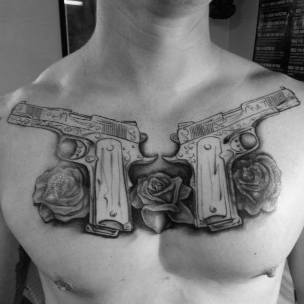 Black and gray chest tattoo featuring two mirrored 1911 pistols with intricate engravings, surrounded by detailed roses for a bold design.