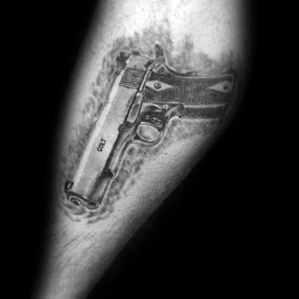 Realistic black and gray tattoo of a Colt 1911 pistol on the forearm, designed with shading to create a three-dimensional effect.