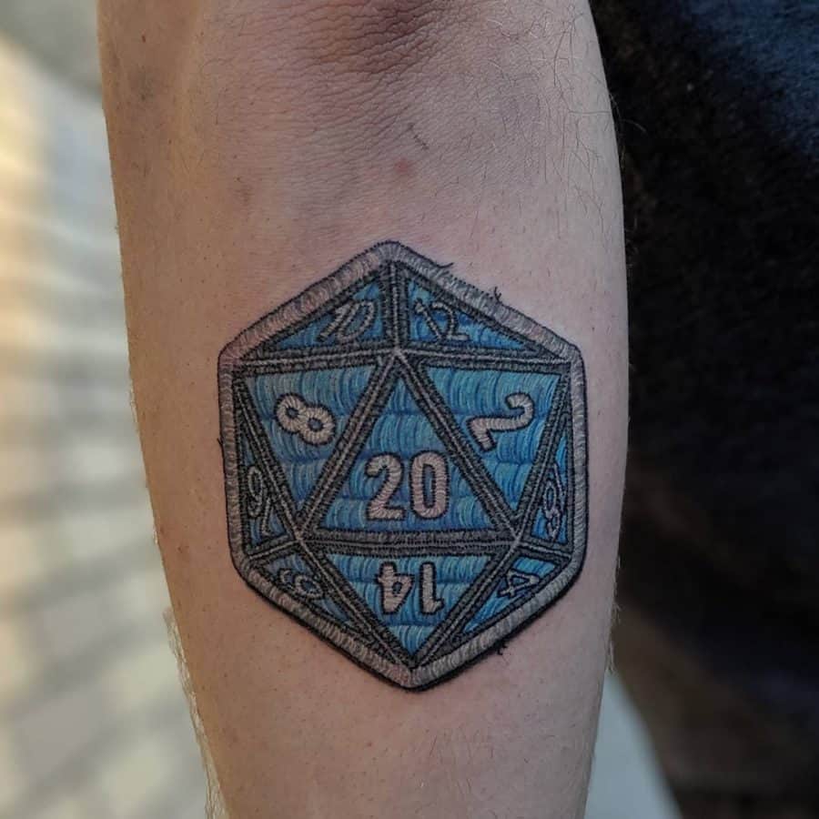 Embroidery-style tattoo of a blue D20 dice, featuring detailed stitched textures for a fabric patch effect.