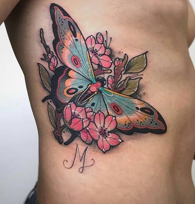 Colorful butterfly tattoo on the side of the torso, featuring vibrant blue and orange wings, pink flowers, and fine black outlines for a bold design.