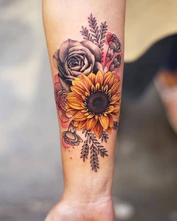 large color and black and grey watercolor tattoo on woman's forearm of a realistic sunflower and roses