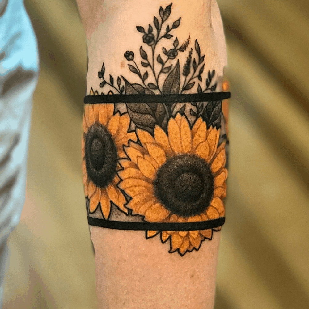 Vibrant sunflower armband tattoo with bold black bands, featuring bright yellow petals and detailed black and grey floral accents.