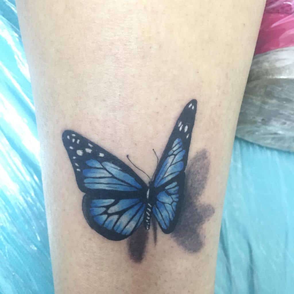 Tattoo of a vibrant blue butterfly with intricate black and white details