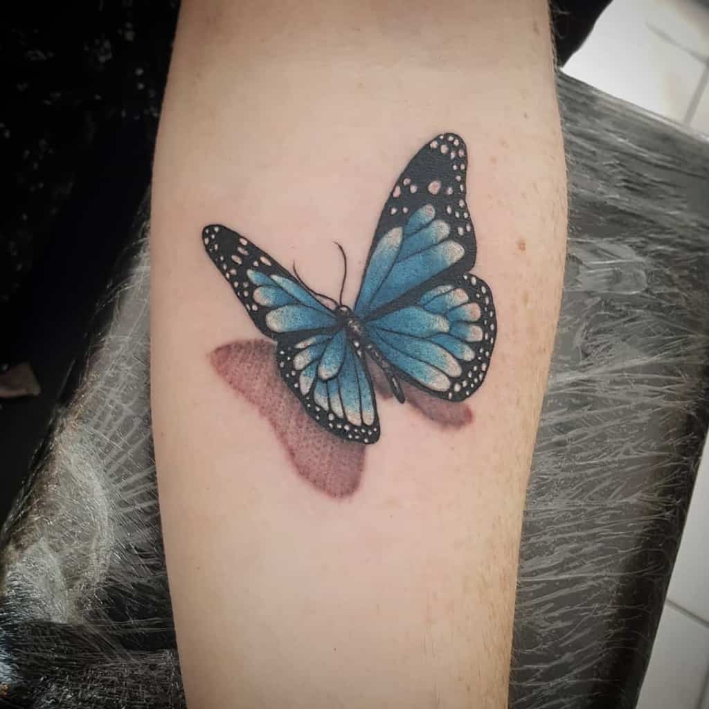 Tattoo of a vivid blue butterfly, casting a delicate shadow on a person's arm