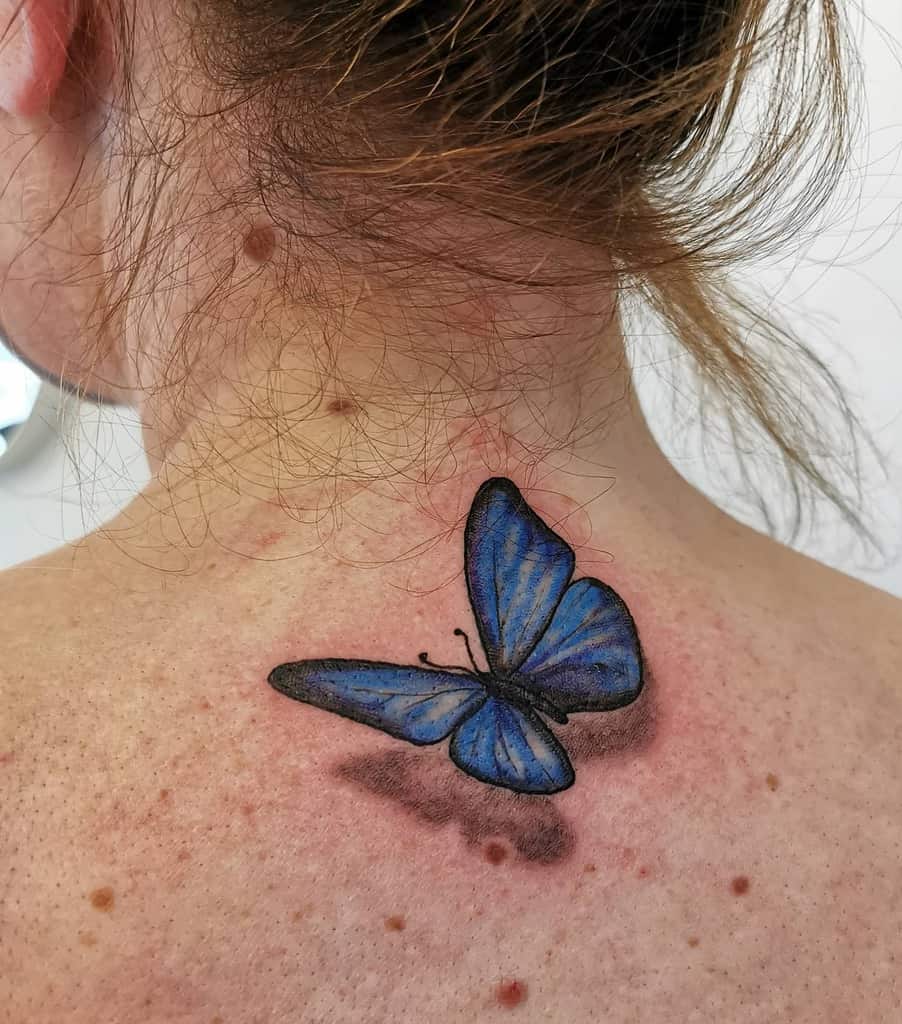 A realistic blue butterfly graces the back of a person's upper neck, its delicate wings creating an enchanting focal point
