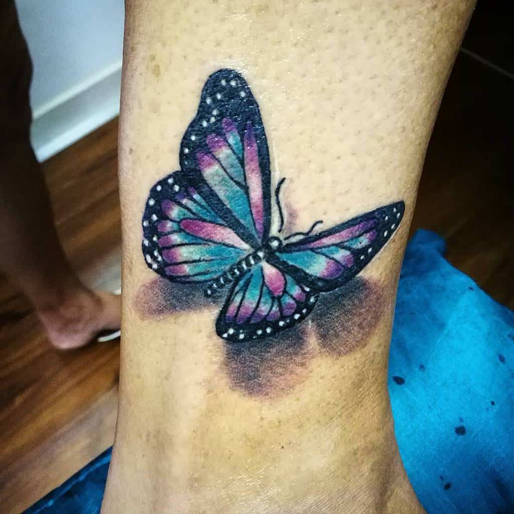 Colorful butterfly tattoo on a person's ankle, featuring blue, pink, and purple wings with white spots
