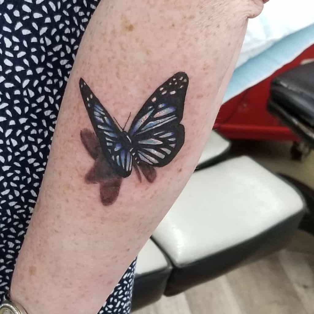 Realistic black and blue butterfly tattoo on an arm, with shadow detail