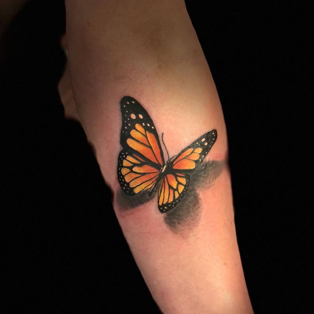 A vibrant monarch butterfly tattoo on an arm, featuring orange and black wings