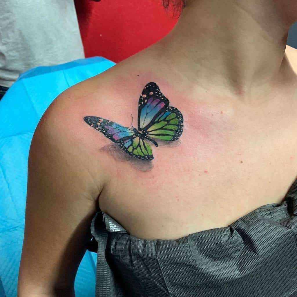 A colorful butterfly tattoo on a person's shoulder, featuring shades of green, blue, and purple