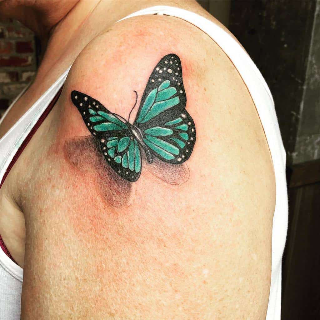 A turquoise butterfly tattoo with black outlines on an upper arm