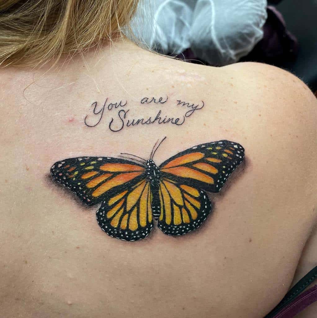 Tattoo of a monarch butterfly under the words "You are my Sunshine" on an upper back