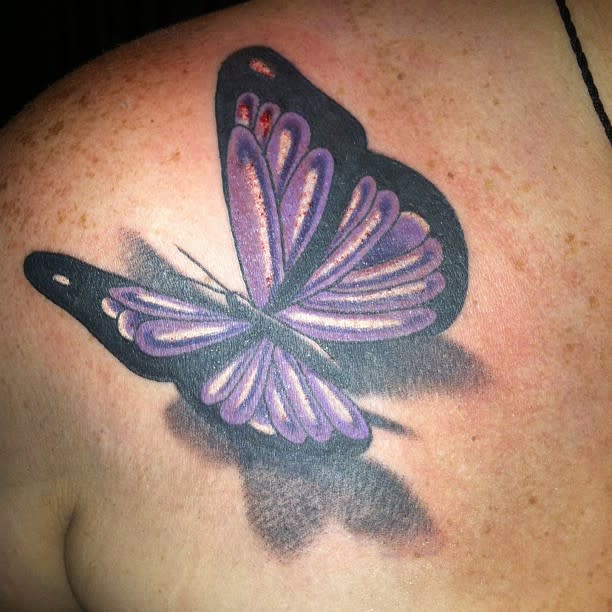A purple and black butterfly tattoo on a shoulder