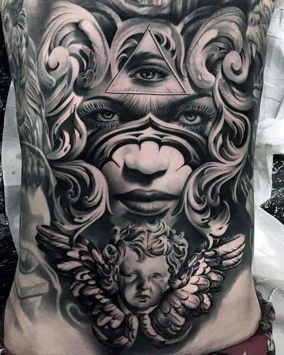Intricate black and gray tattoo of a face with an eye in a triangle, surrounded by swirling patterns and an angelic cherub below