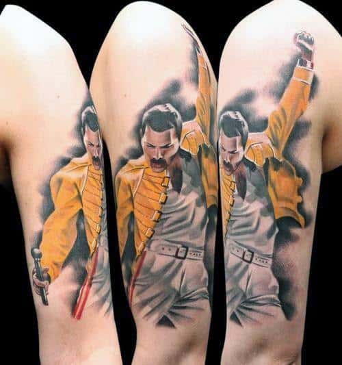 Freddie Mercury tattoo in iconic yellow jacket pose with fist raised, detailed realism style across upper arm.