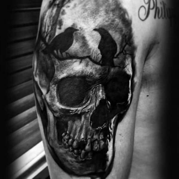 Realistic skull tattoo with two black crows perched on branches, creating a dark and mysterious upper arm design.