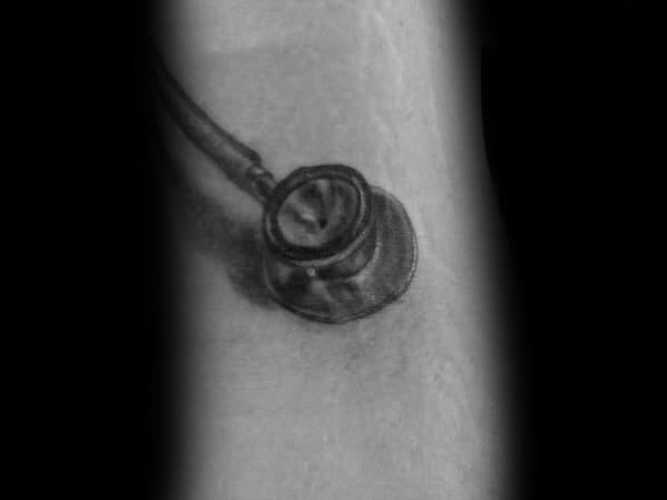 Realistic stethoscope tattoo on the arm, designed to look like it’s pressed against the skin, symbolizing dedication to medicine.