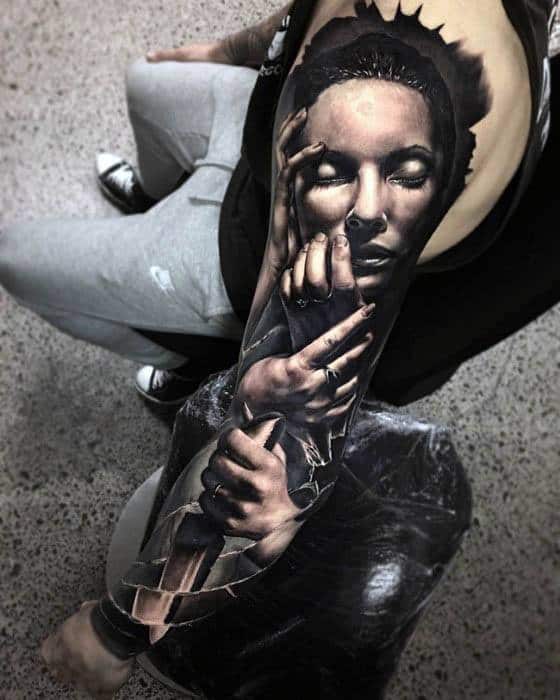 Realistic broken glass tattoo of a woman's face and hands on a full sleeve, blending photorealism with surreal cracked effects.