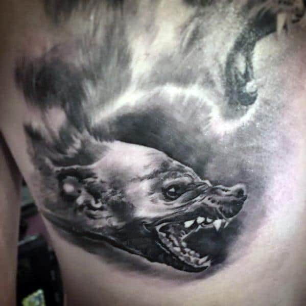 Realistic black and grey hyena tattoo on the side torso, showcasing sharp teeth and a fierce snarl with smoky shading for dramatic depth.