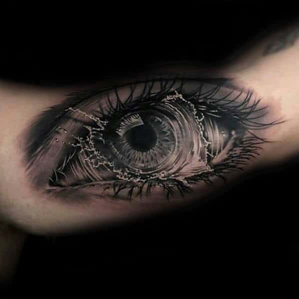 Realistic tattoo of an eye with intricate detailing and eyelashes, surrounded by dark shading on a light skin canvas
