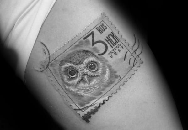 A beautifully inked tattoo of a postage stamp graces the skin, intricately featuring a detailed owl design