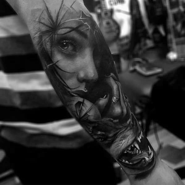Black and white tattoo of a woman's face with spider web and snarling animal on a person's forearm