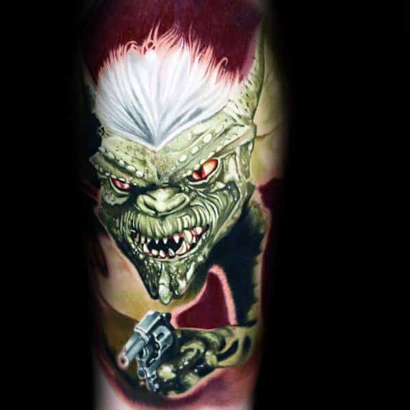 Realistic Gremlin tattoo with fierce red eyes, sharp teeth, and a gun, featuring bold shading and striking details.