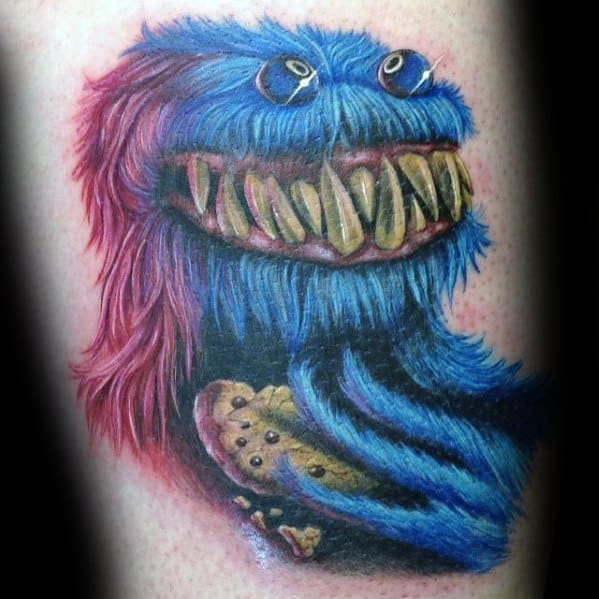 Colorful Cookie Monster tattoo with sharp monster teeth, holding a cookie, featuring wild blue and red fur with big eyes.
