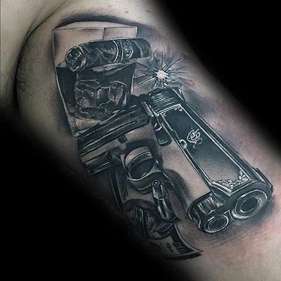 Realistic black and gray tattoo of a 1911 pistol with a glass of whiskey, cigar, dollar bills, and a bullet impact design.