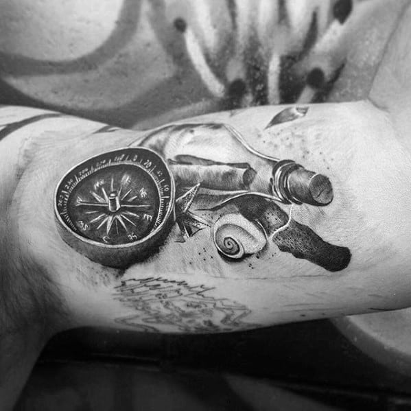 Tattoo of a compass, shell, and rope with a message in a bottle on a person's biceps