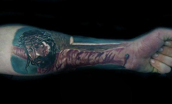 Forearm tattoo of Jesus on the cross, detailed with crown of thorns and nails