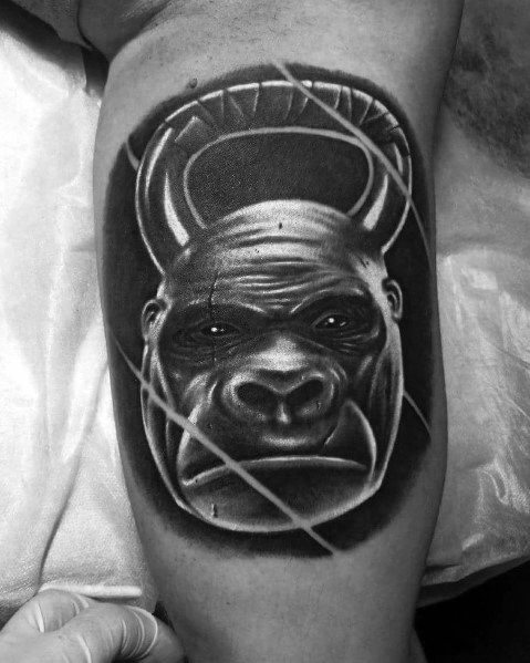 Realistic black and gray tattoo of a gorilla’s face fused with a kettlebell, symbolizing strength, power, and determination in fitness and CrossFit.