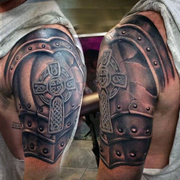 Tattoo of Celtic cross and armor on upper arm and shoulder, featuring intricate designs and shading for a 3D effect