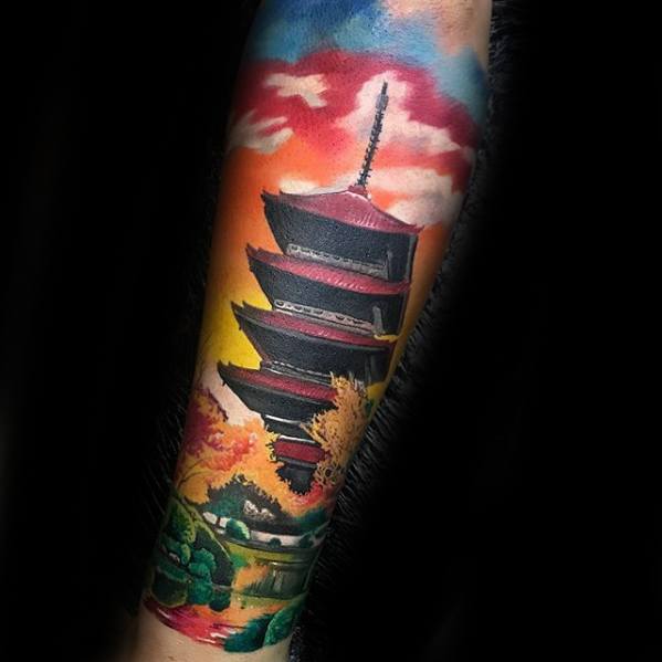 Colorful forearm tattoo of a Japanese pagoda with vibrant sunset sky, autumn trees, and a serene landscape scene.
