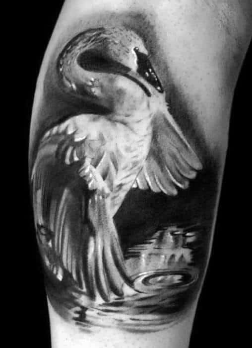 Black and white swan tattoo with wings partially lifted, gazing at its reflection in calm rippling water for a serene effect.
