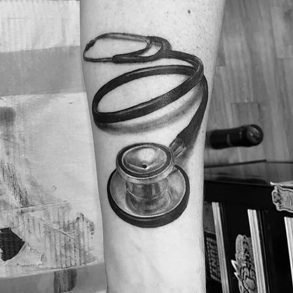 Detailed black and gray stethoscope tattoo on the forearm, featuring a realistic design that highlights medical passion and dedication.