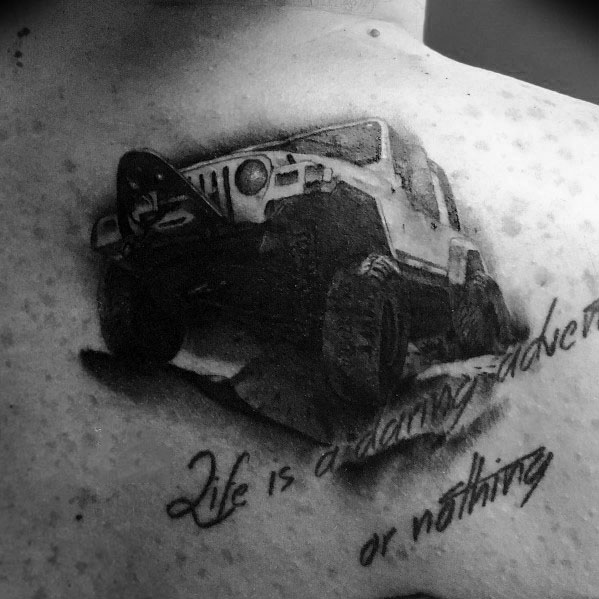 Black and grey Jeep tattoo on upper chest, featuring an off-road Jeep with bold text that reads Life is daring adventure or nothing.