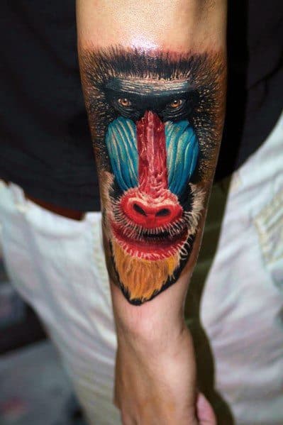 Hyper-realistic baboon tattoo on forearm with vivid blue and red facial features, lifelike fur texture, and piercing eyes for a bold look.