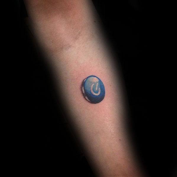 Minimalist 3D power symbol tattoo on the forearm, designed to look like a small, raised blue button.