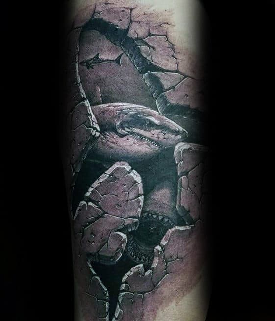 Tattoo of a shark breaking through cracked, realistic skin on a forearm, creating a 3D effect with dark shading and detail