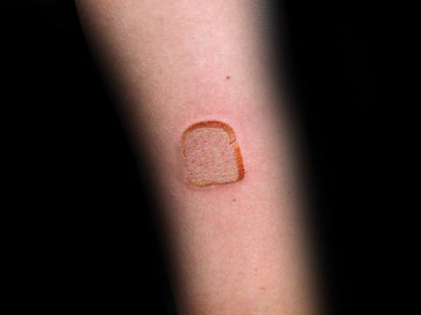 Small toasted bread tattoo on a person's forearm with a simple design and light shading, creating a minimalist and unique look.