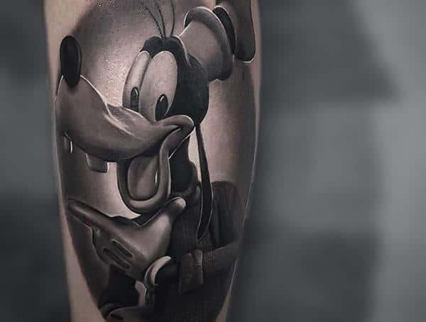 Black and grey realism tattoo of a cartoon dog character with detailed shading and depth, showcasing a classic tattoo style.