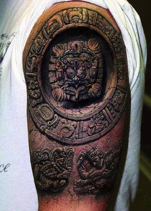 A detailed arm tattoo featuring Aztec-inspired designs and symbols, including a circular emblem and intricate patterns