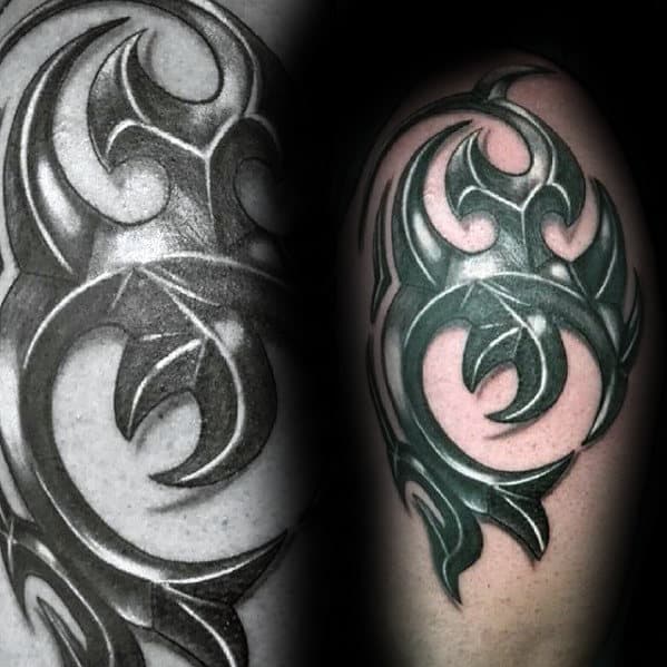 Black and green tribal-style tattoo on a person's upper arm, featuring bold, abstract shapes with curving lines