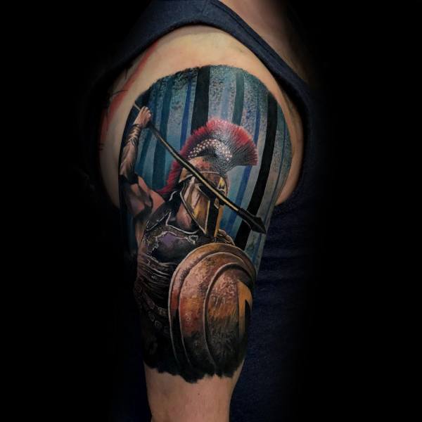 Vibrant upper arm tattoo of a Spartan warrior mid-battle, wielding a spear and bronze shield, set against a dramatic forest backdrop.