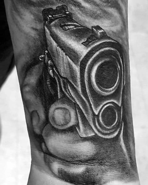 Black and gray tattoo of a 1911 pistol being aimed forward, creating a bold perspective with detailed shading for a realistic effect.