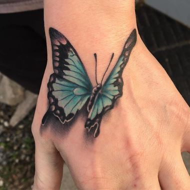 Realistic blue butterfly tattoo on the hand with a 3D shadow effect, creating a lifelike and striking appearance.