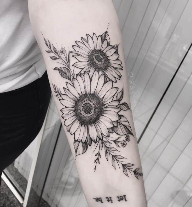 Black and grey sunflower tattoo on upper arm featuring two large blooms with fine line details, bold shading, and delicate leaves.