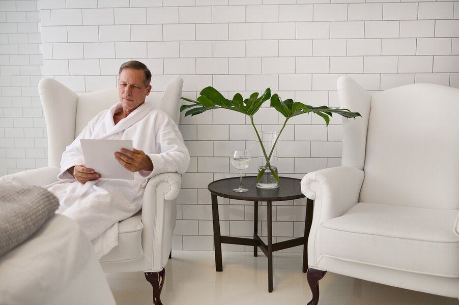 Man in a white robe reads a document about men's wellness near a table with water and green leaves